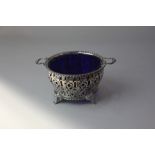 A George VI pierced silver two handled circular dish with blue glass liner on four scroll feet,