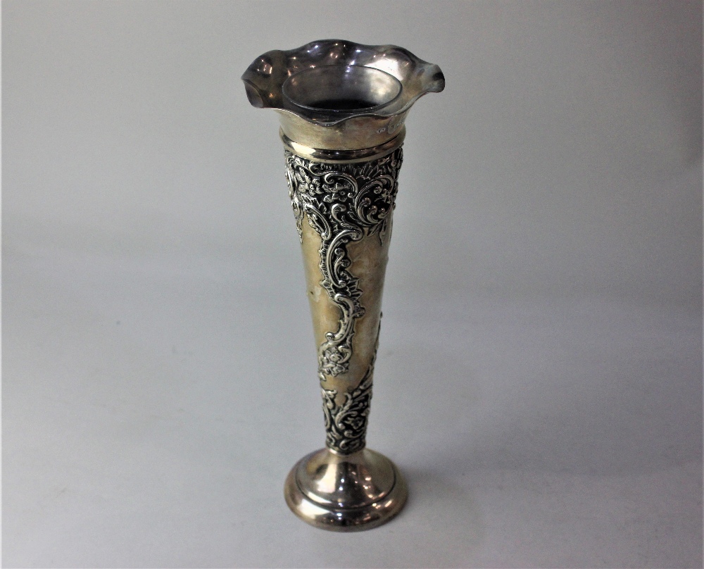 A late Victorian silver trumpet shape vase with embossed scrolls and flowers and circular base,