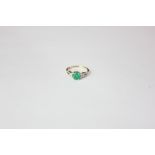 An emerald and diamond ring claw set with a round emerald between pave set diamond pierced shoulders