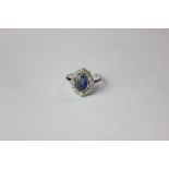 A sapphire and diamond ring the stone rubover set within a diamond border in 18ct white gold