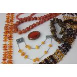 A pale brown hardstone necklace; two amber necklaces; an oval silver mounted cornelian brooch; a