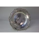 An Edward VII silver circular dish with shaped cast border of trophies and ribbons, engraved