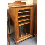 An Edwardian inlaid music cabinet single glazed door enclosing shelves on plinth base with castors