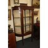 An Edwardian mahogany display cabinet with curved glass sides and glazed panel door enclosing fabric