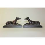 A pair of bronzed metal models of recumbent greyhounds, 17cm long