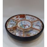An Oriental lazy Susan with seven ceramic sectional dishes decorated with landscapes, in black