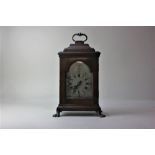 An 18th century style walnut mantle clock with arched steel dial, cushion top and handle on four