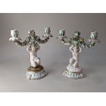 A pair of German porcelain candelabra, each modelled as a cherub holding two flower encrusted
