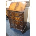 A reproduction mahogany bureau with four serpentine shaped drawers and drop ring handles on