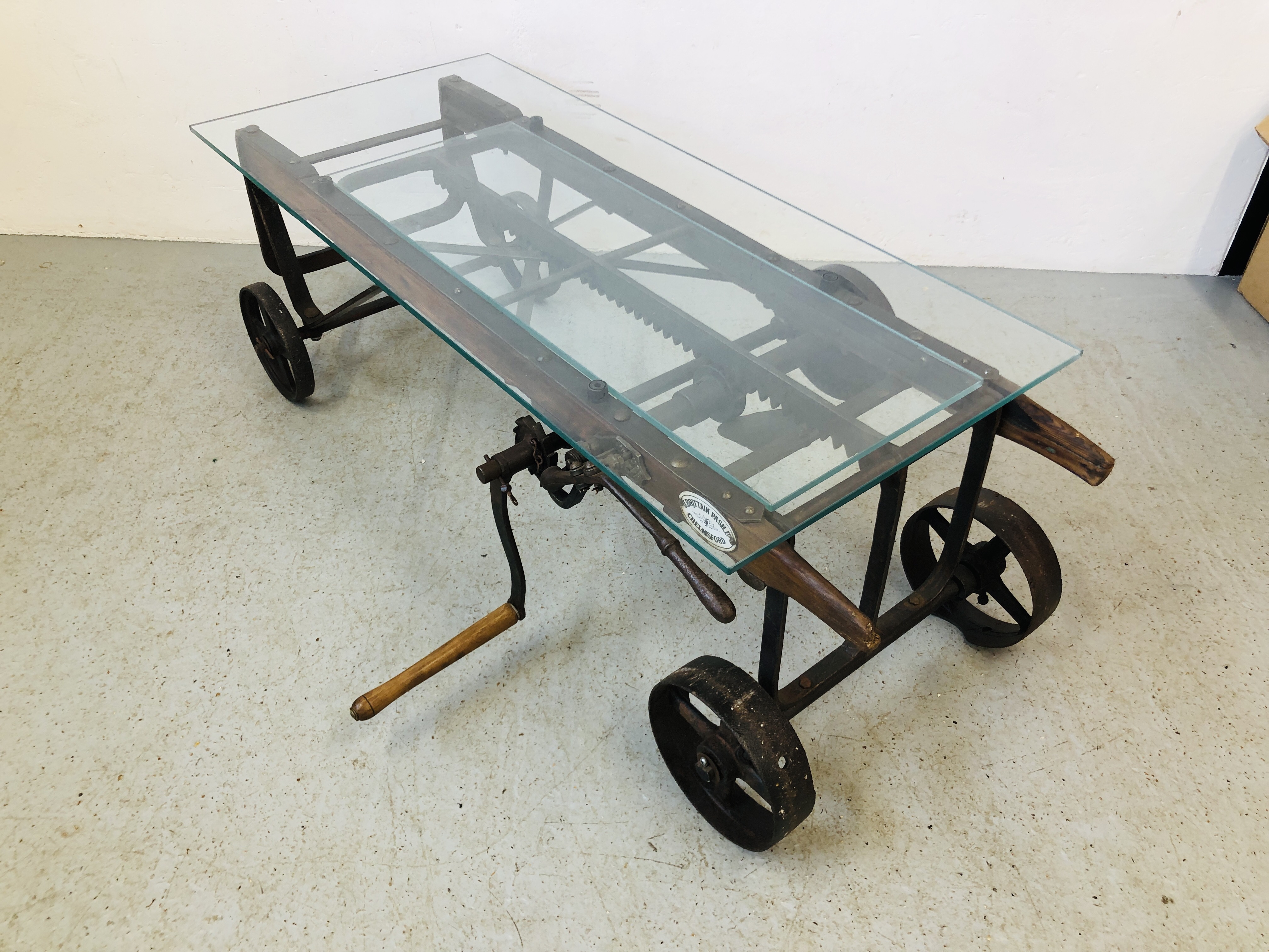 A GLASS TOP EXTENDING COFFEE TABLE CONVERTED FROM AN ANTIQUE COOKS RATCHET ACTION SACK BARROW