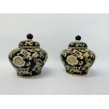 A PAIR OF COVERED VASES THE CREAM DECORATION ON A BLACK GROUND HEIGHT 23CM