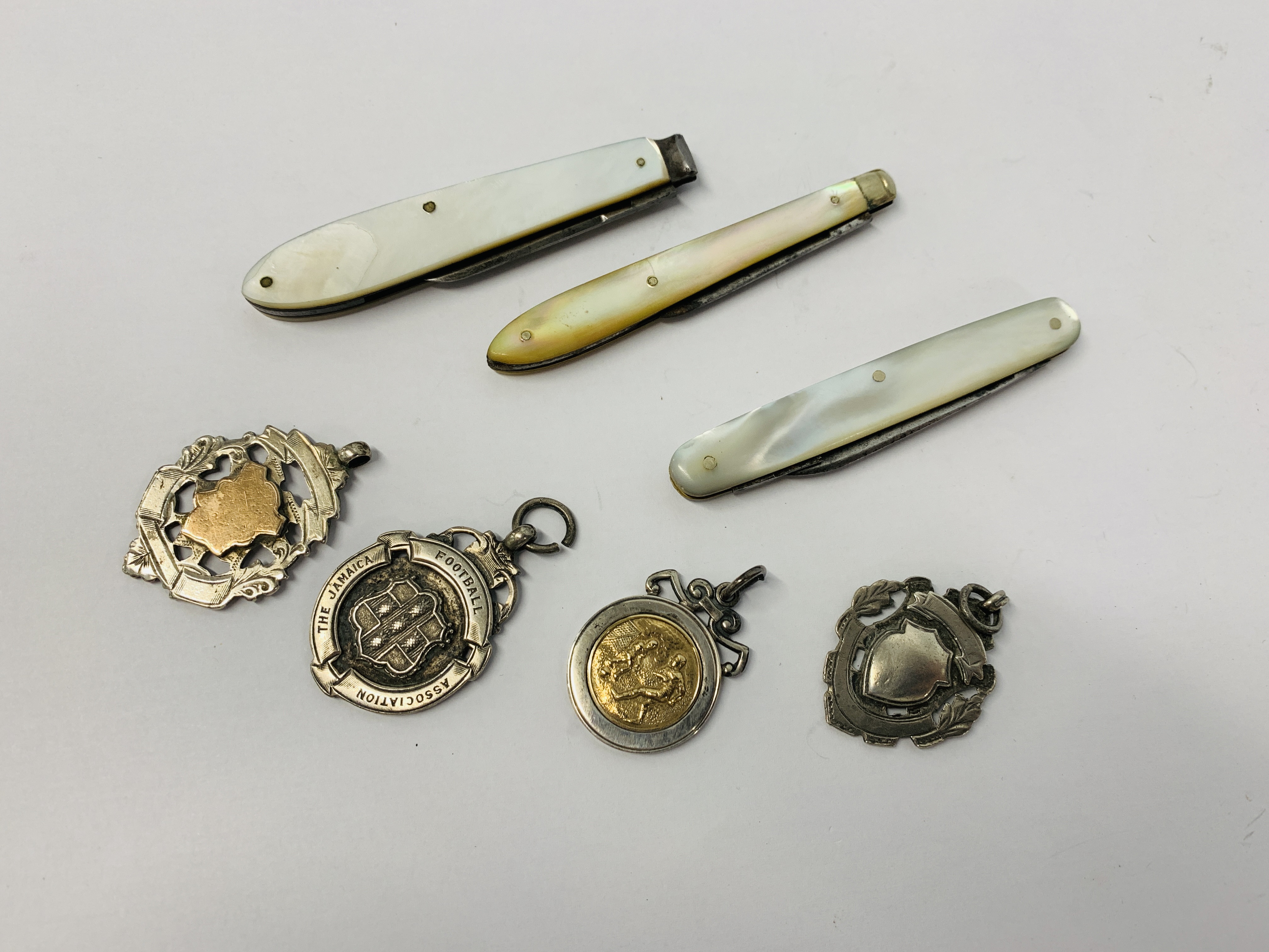 THREE MOTHER OF PEARL HANDLED FRUIT KNIVES AND FOUR SILVER FOOTBALL MEDALS