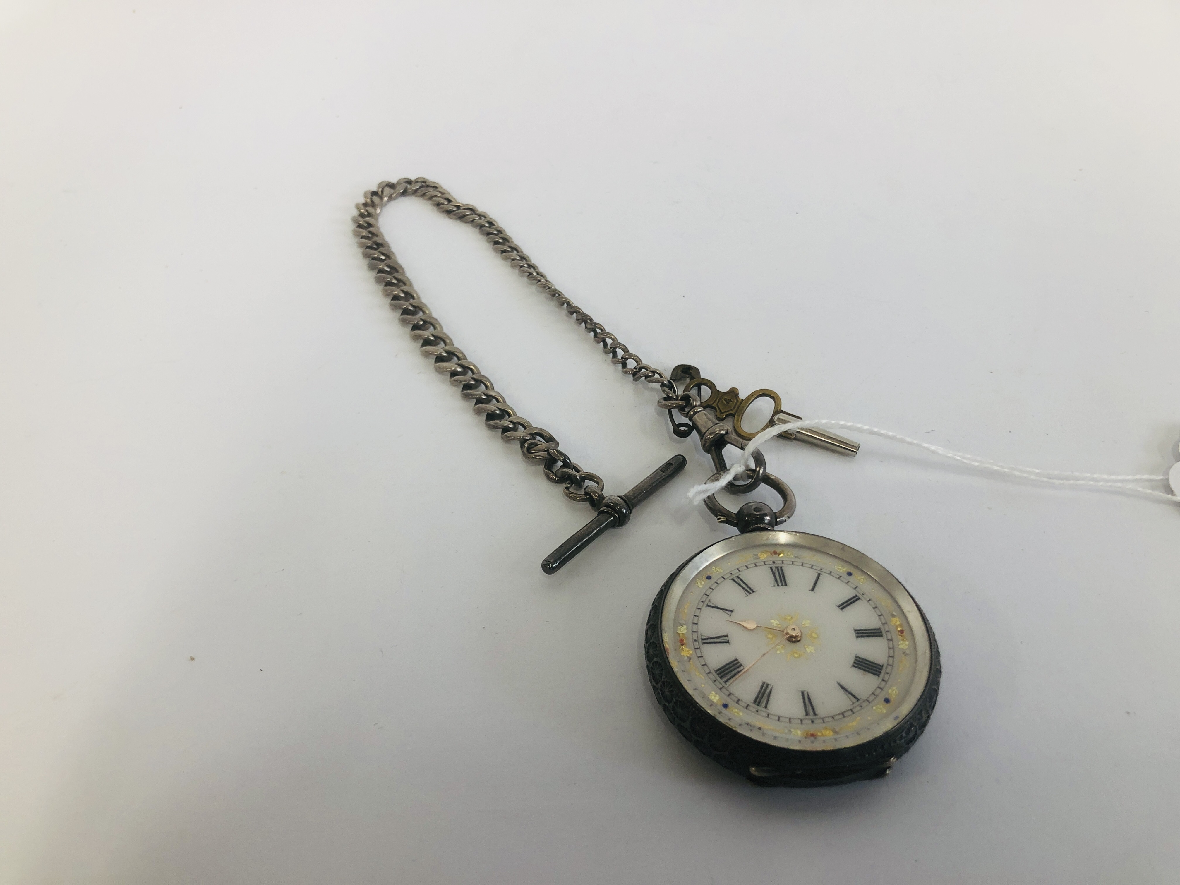 AN ORNATE SILVER POCKET WATCH WITH DECORATIVE ENAMELLED FACE ON SILVER T-BAR CHAIN