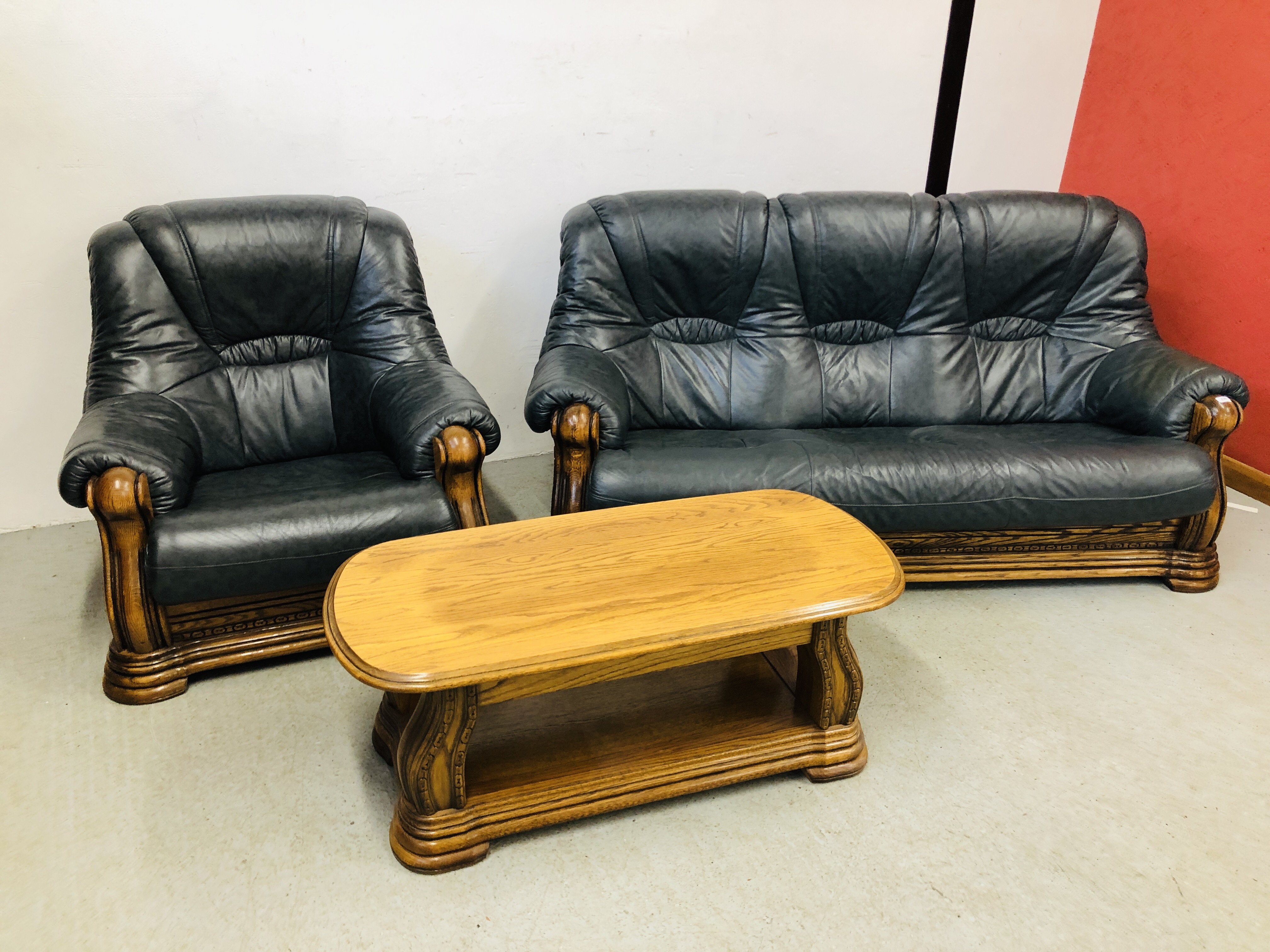 A NAVY BLUE 3 SEATER SOFA AND ARM CHAIR WITH CARVED WOOD SURROUND AND MATCHING OAK COFFEE TABLE