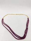 18CT GOLD TRIPLE STRAND NECKLACE SUSPENDING A TRIPLE STRAND RUBY STYLE BEADED NECKLACE