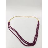 18CT GOLD TRIPLE STRAND NECKLACE SUSPENDING A TRIPLE STRAND RUBY STYLE BEADED NECKLACE