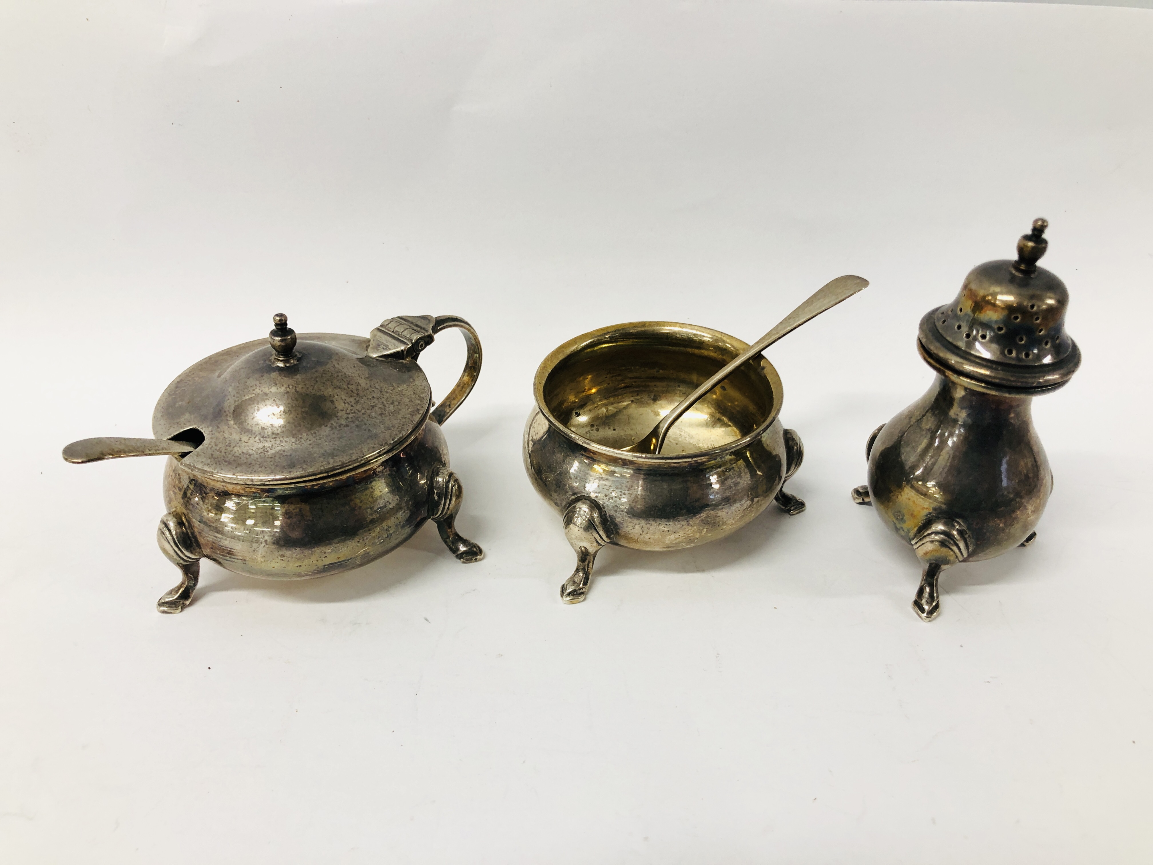 A SILVER TRIPOD PEPPER, MATCHING MUSTARD POT & SALT COMPLETE WITH SPOONS,