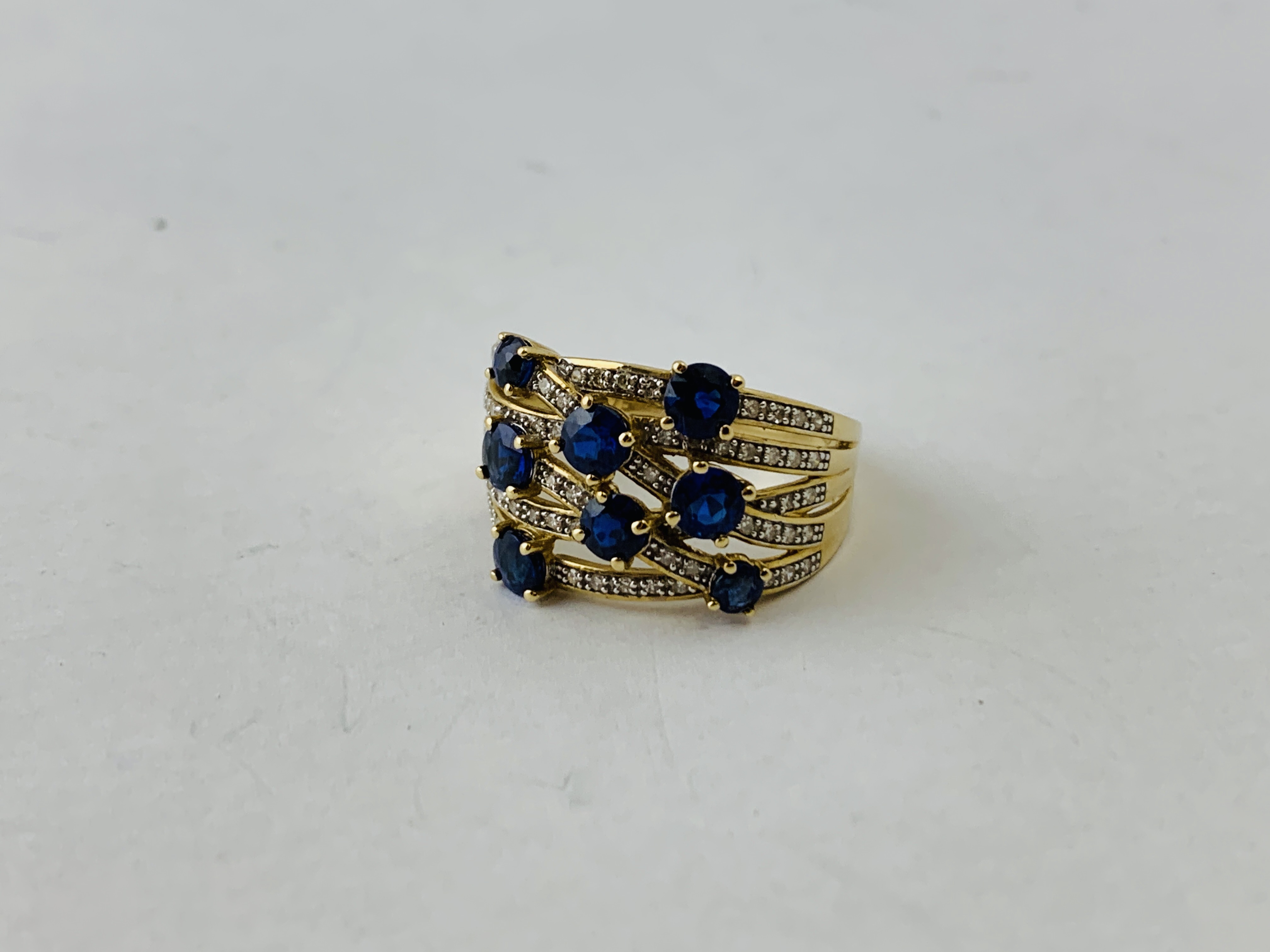 A 9CT GOLD DESIGNER WOVEN STRAND RING SET WITH 8 PRINCIPAL BLUE STONES THE STRANDS ENCRUSTED WITH