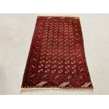 A MID 20TH CENTURY TURKOMAN RED PATTERNED RUG 122CM. X 194CM.