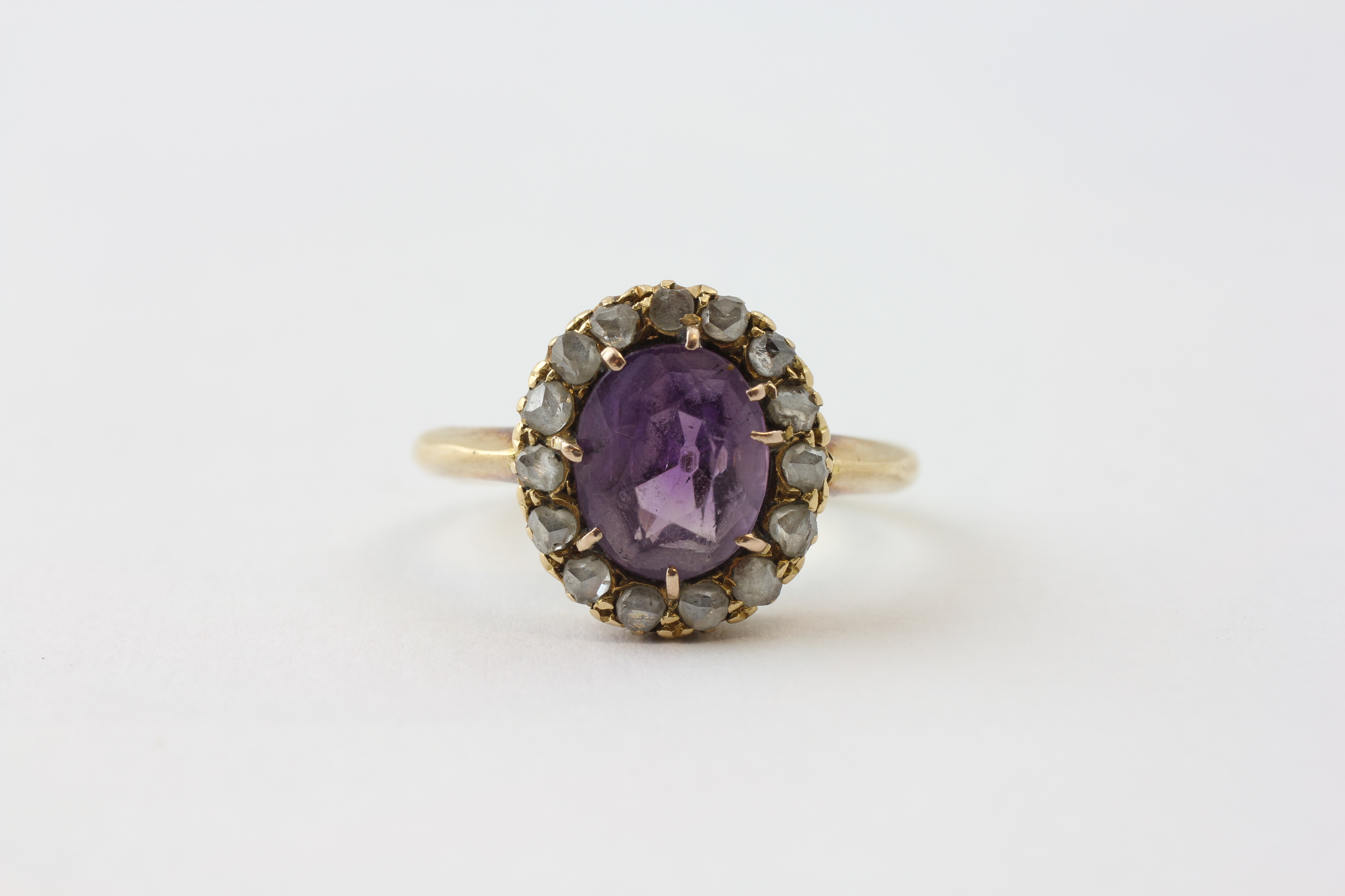 AN AMETHYST RING, THE OVAL STONE SURROUNDED BY FIFTEEN SMALL DIAMONDS SET IN YELLOW METAL,