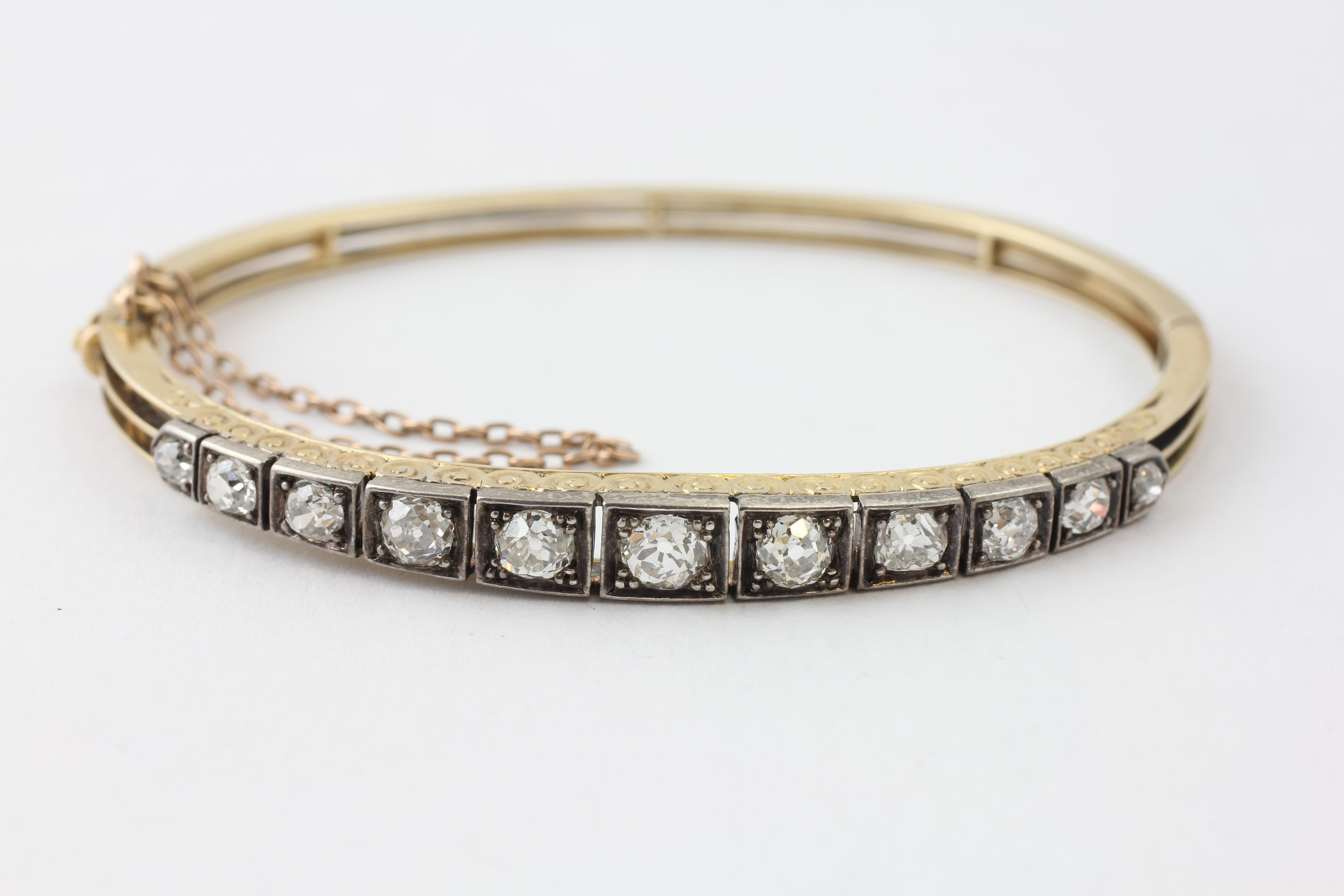 AN ELEVEN STONE DIAMOND HINGED BANGLE WITH SAFETY CHAIN,