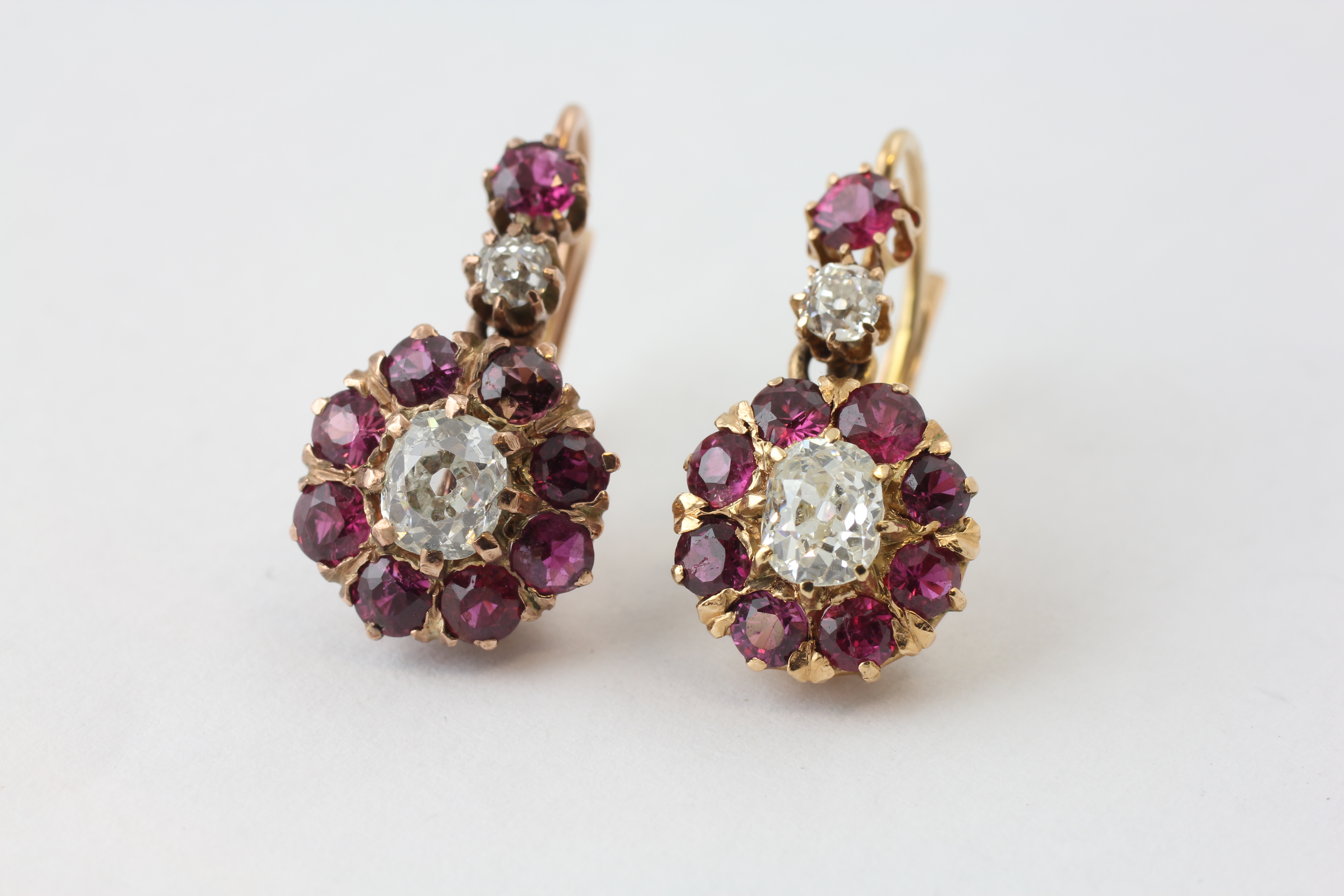 A PAIR OF DIAMOND EARRINGS, THE CENTRAL OLD CUT STONE SURROUNDED BY SMALL MAUVE STONES,