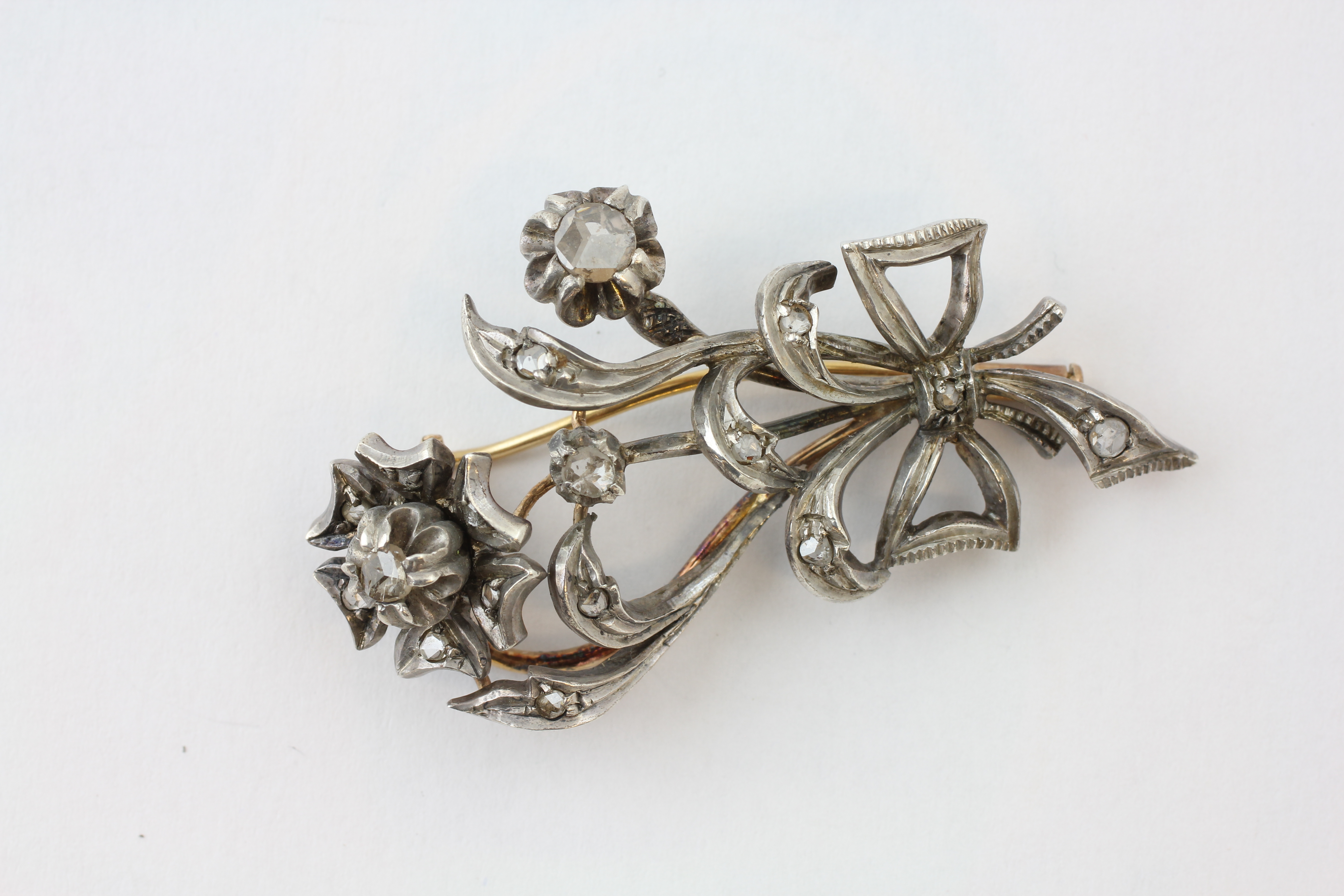 AN EDWARDIAN DIAMOND BROOCH OF FLOWERHEAD AND BOW DESIGN SET IN WHITE AND YELLOW PRECIOUS METAL,