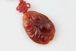 AN ORIENTAL CARVED HARD STONE PENDANT ON CORD OF NATURALISTIC DESIGN,