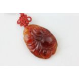 AN ORIENTAL CARVED HARD STONE PENDANT ON CORD OF NATURALISTIC DESIGN,