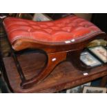 A mahogany foot stool upholstered in faux red leat