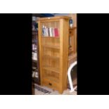 A modern oak bookcase with five shelves and one dr