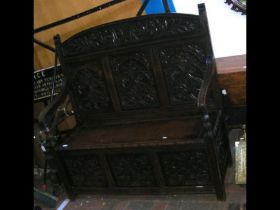 An antique carved oak settle with hinged seat