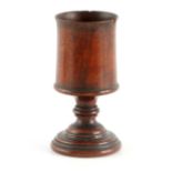 AN 18TH CENTURY TURNED WALNUT TREEN CUP of tapering form with turned pedestal foot 13.5cm high.