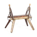 A 19TH CENTURY HARDWOOD CAMEL STOOL with raised open-work sides and brass finials, mounted with