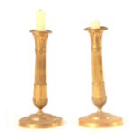 A PAIR OF 19TH CENTURY FRENCH EMPIRE GILT BRASS CANDLESTICKS of classical form with leaf cast scones