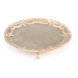 A GEORGE III SILVER SALVER with reed-edged border and embossed floral swags, raised on three ball