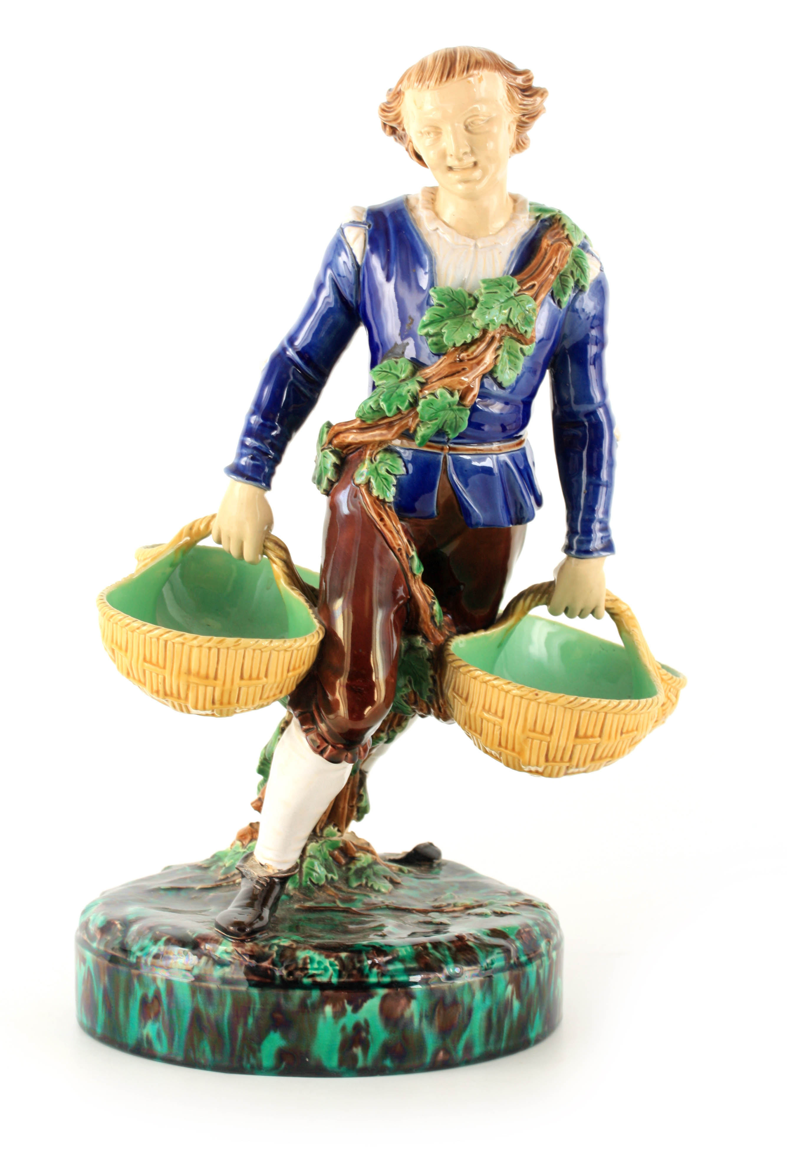 A 19TH CENTURY MINTON MAJOLICA FIGURE finely modelled as a young man carrying baskets coloured in