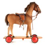 A LATE 19TH/EARLY 20TH CENTURY HIDE COVERED WOOD FIGURE OF A CHILD'S HORSE on a wheeled base with
