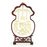 A CHINESE CARVED JADE HANGING PENDANT mounted on a silver wire inlaid hardwood stand, depicting a