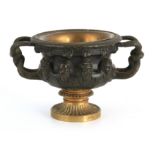 A 19TH CENTURY FRENCH BRONZE AND GILT BRONZE URN with relief cast mask heads and entwined handles;