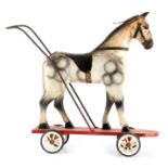 A 19TH CENTURY PAINTED DAPPLED CARVED WOOD CHILD'S PUSH TOY HORSE on wheeled base with ironwork