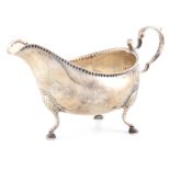 A GEORGE III IRISH SILVER SAUCE BOAT with scroll handle and bead edge border to the rim, on three