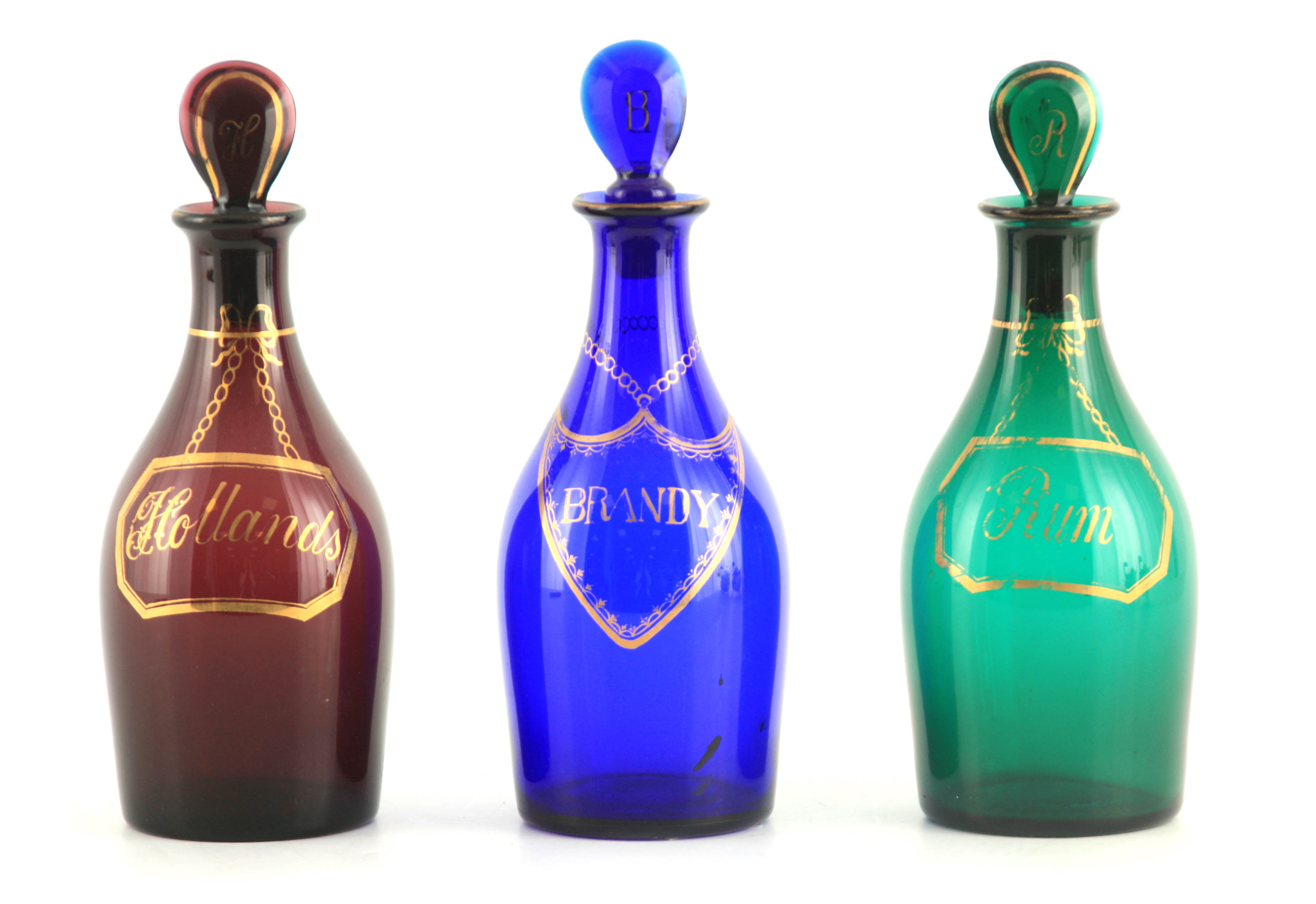 A MATCHED SET OF THREE LATE GEORGIAN COLOURED SPIRIT DECANTERS with gilt work labels for Rum,