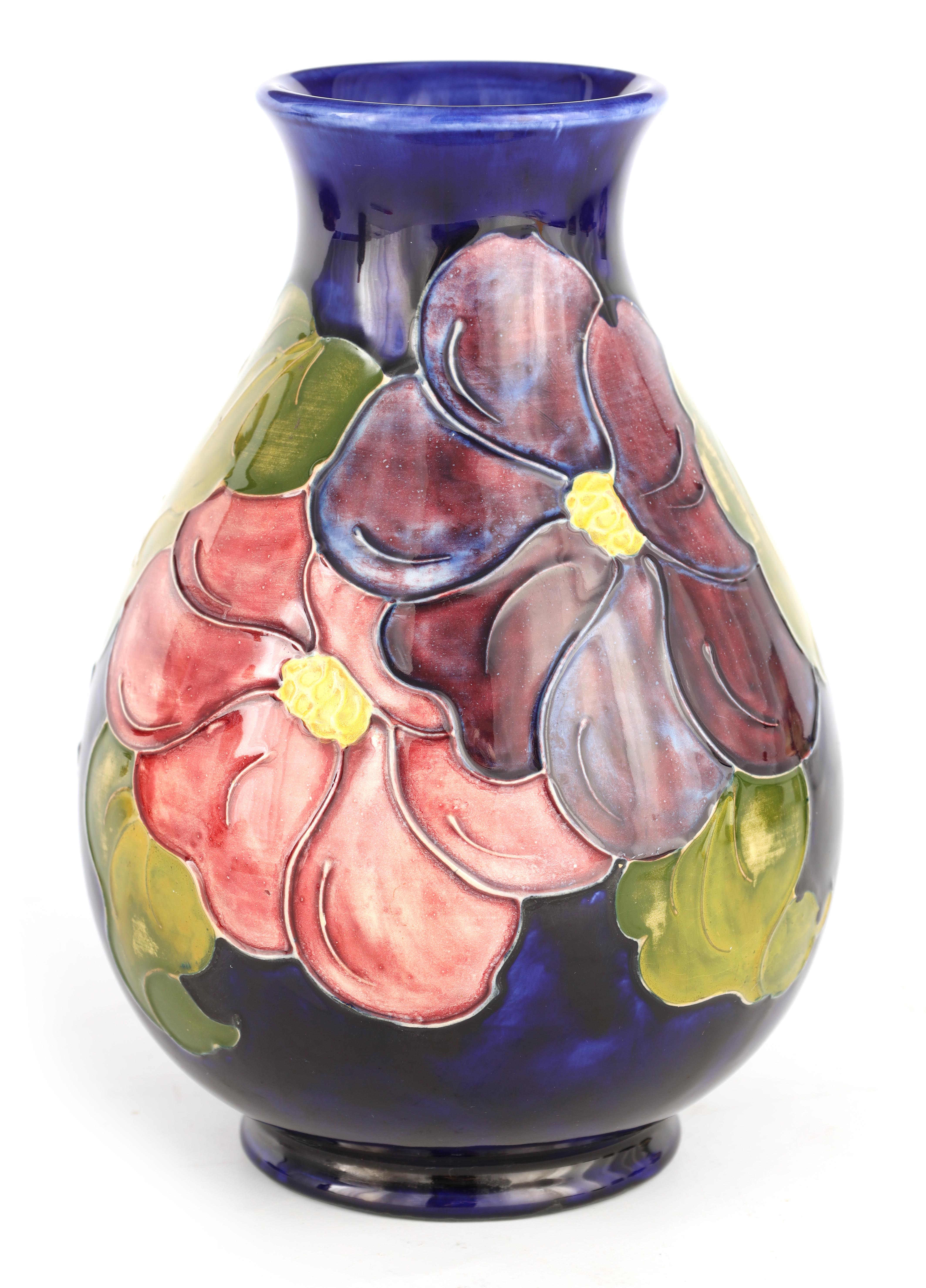 A WALTER MOORCROFT FOOTED OVOID VASE decorated in the Clematis pattern on a dark blue mottled