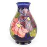 A WALTER MOORCROFT FOOTED OVOID VASE decorated in the Clematis pattern on a dark blue mottled