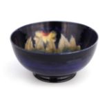 A MOORCROFT BURSLEM FOOTED BOWL decorated in the Big Pansy pattern on a dark mottled blue ground,