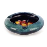 A MOORCROFT CIRCULAR ASHTRAY WITH CURVED RIM decorated with a Freesia spray on a dark mottled blue-