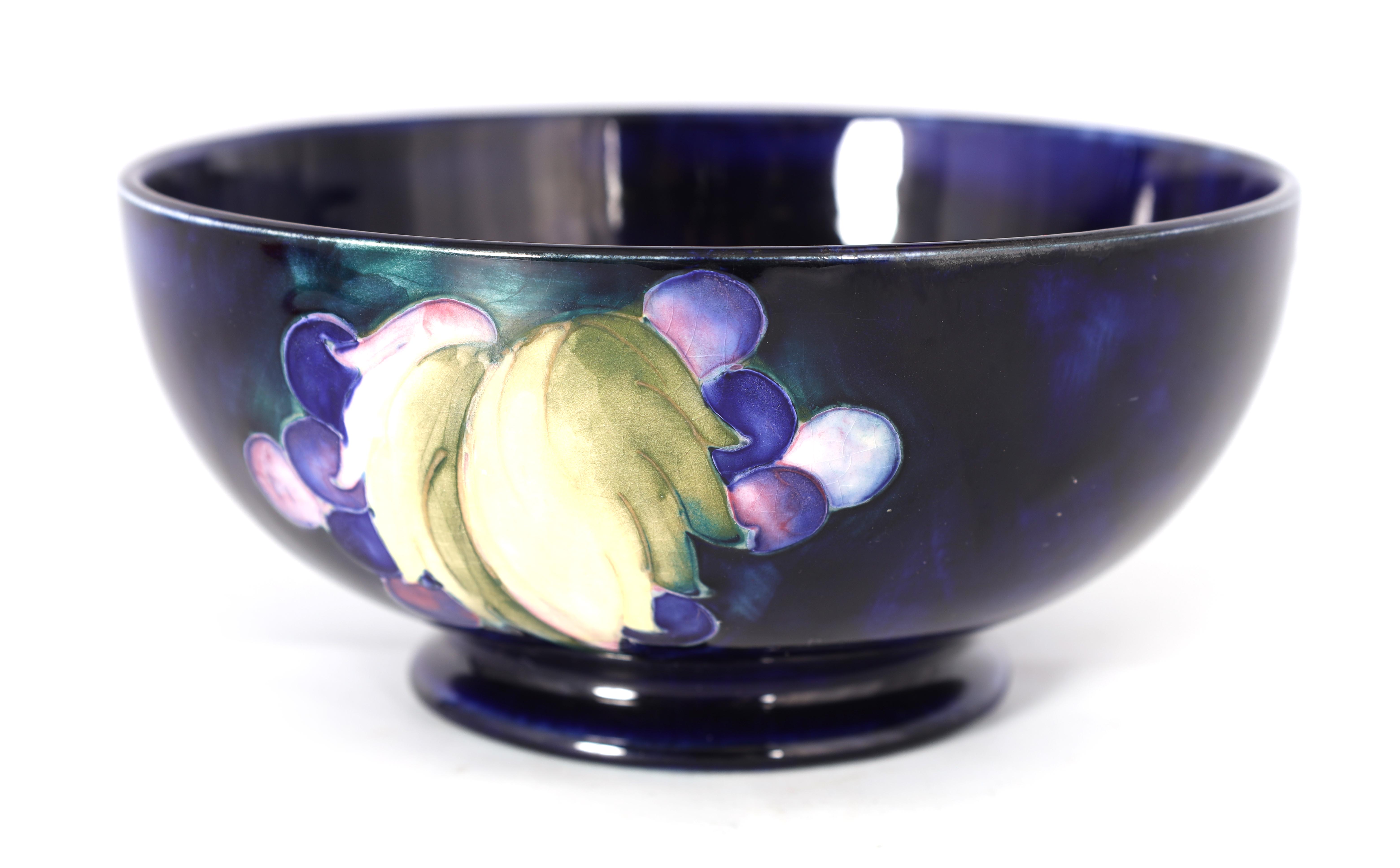 A 1930S MOORCROFT FOOTED BOWL decorated in the Leaf and Berry pattern on a dark mottled blue ground,