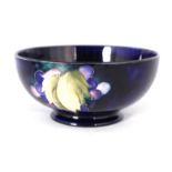 A 1930S MOORCROFT FOOTED BOWL decorated in the Leaf and Berry pattern on a dark mottled blue ground,