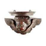 A 17TH CENTURY CARVED OAK WINGED CHERUB HEAD WALL BRACKET with later moulded top 36cm wide 22.5cm